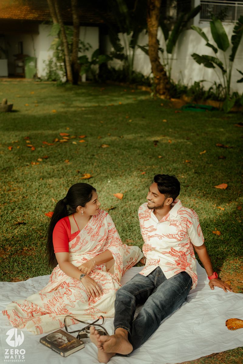 Couple relaxing on white blanket having picnic in garden with fallen autumn leaves on grass.