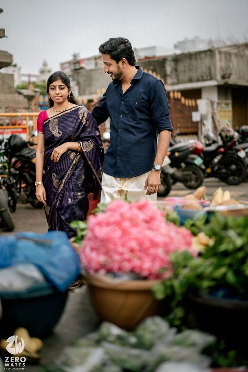 A couple shops at an outdoor flower market with vibrant pink blooms in the foreground.