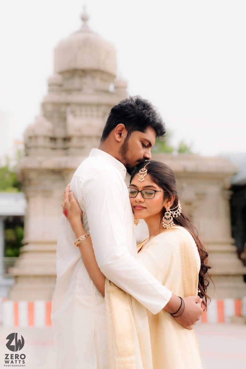 Couple in white traditional dress share tender moments at a temple with architectural pillars in the background.