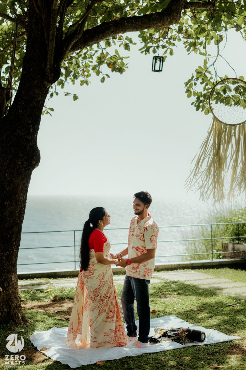 A romantic seaside photo session with a couple on a white blanket under a majestic tree.