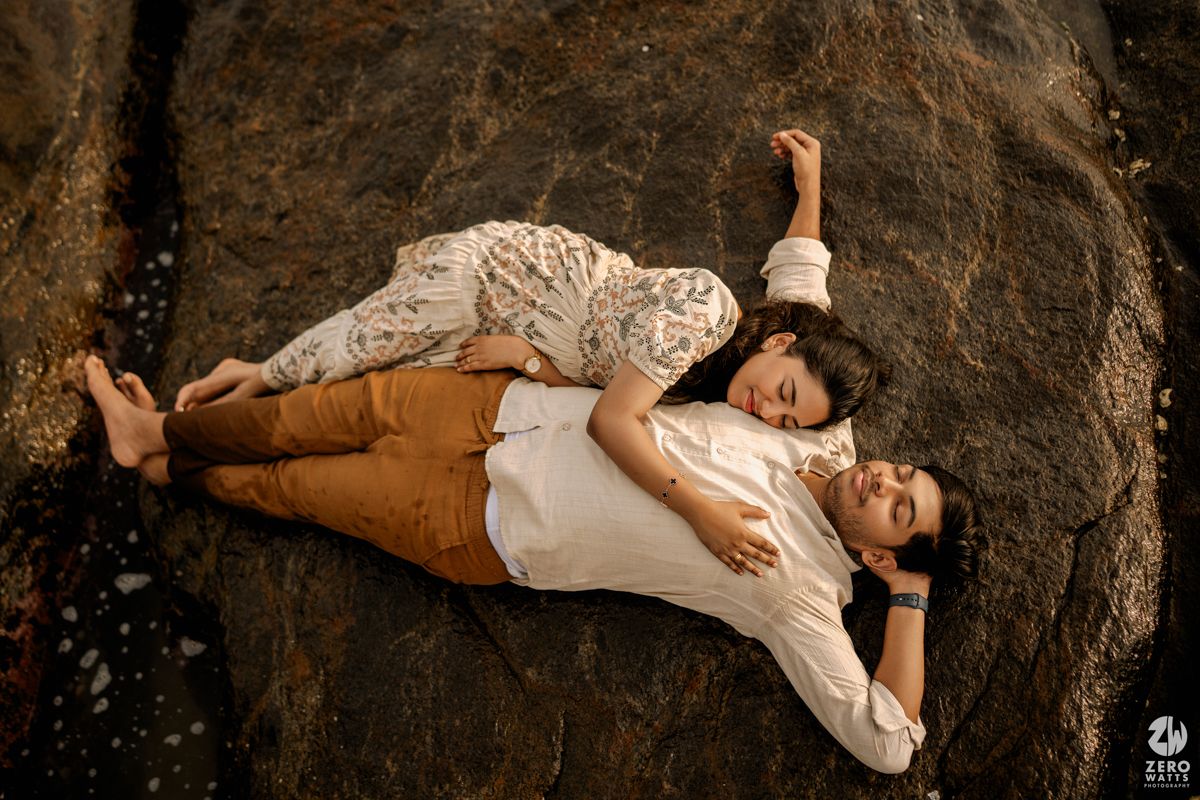 A couple in casual attire resting together on rugged coastal rocks.