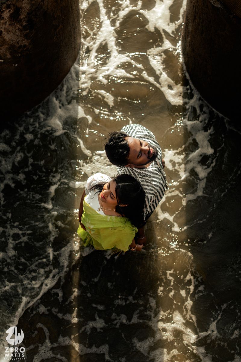 Artistic overhead shot of a couple in traditional attire posing on wet sand.
