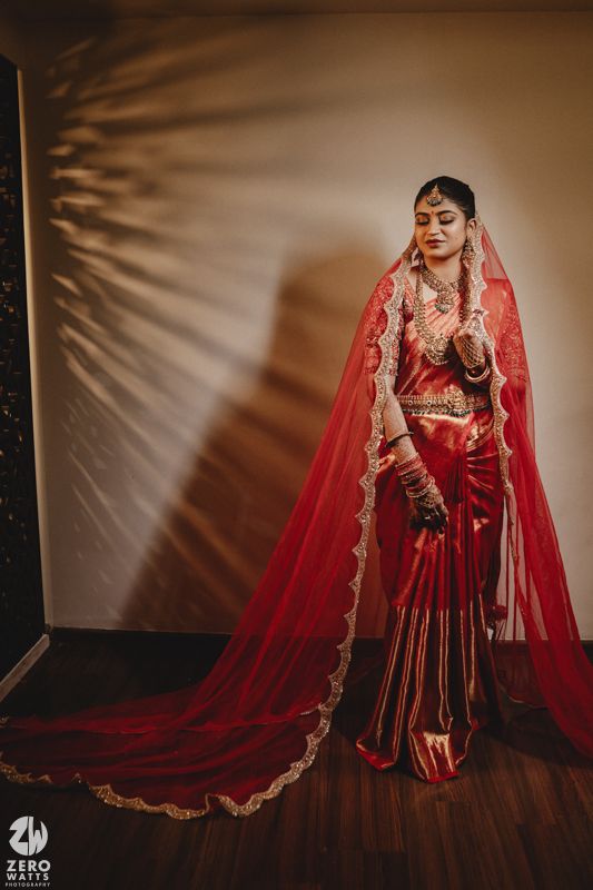Traditional Indian bride in red lehenga and veil poses elegantly against dark backdrop in artistic bridal portraits.