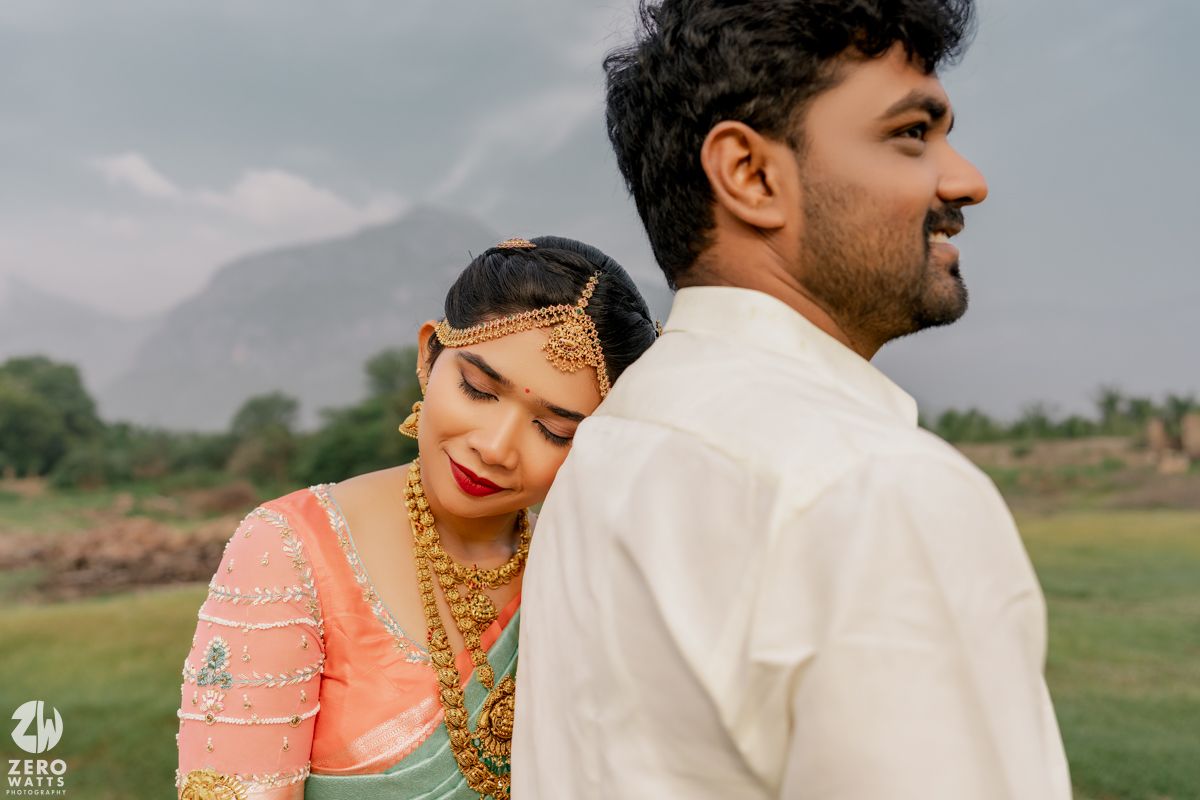 Indian bride in pink saree leans on groom shoulder outdoors during traditional wedding photoshoot.