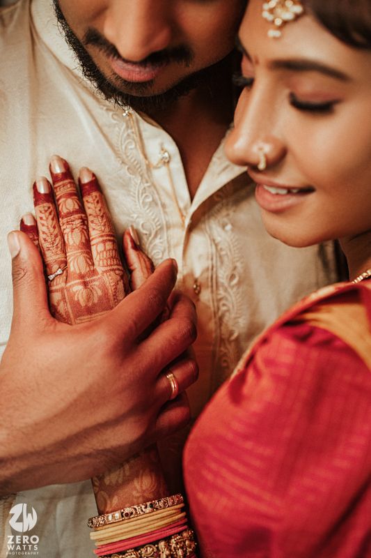 Close-up of Indian couple's hands with intricate mehndi and gold rings during traditional South Indian wedding ceremony.