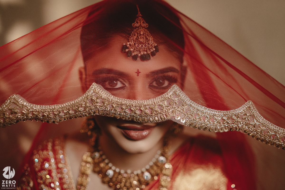 A close-up detail of traditional Indian bridal jewelry and red wedding attire with intricate embellishments and embroidery.