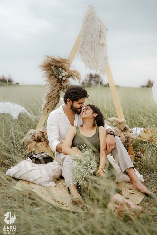 Romantic outdoor picnic setup with pampas grass and white fabric backdrop in a dreamy meadow setting.