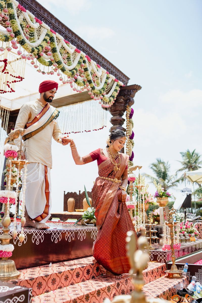 Outdoor wedding mandap with floral decorations and palm trees visible in the tropical background.