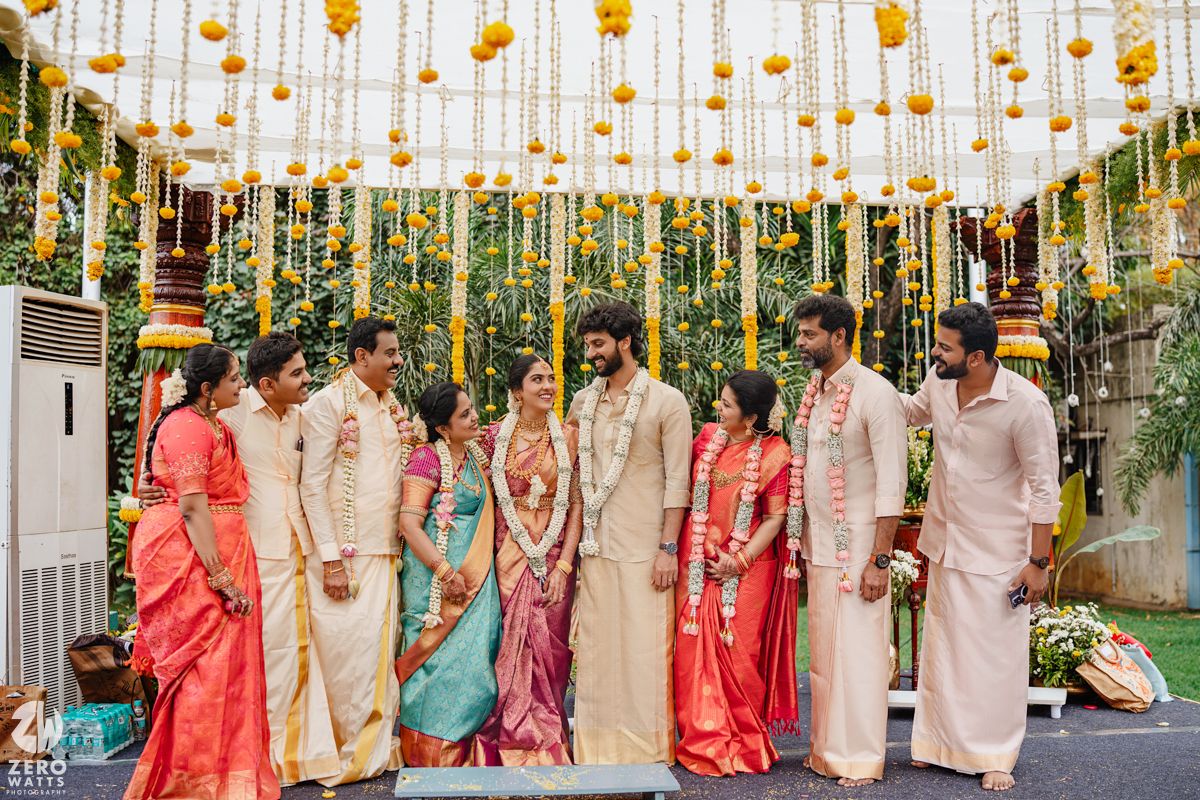 Group photo under marigold and string decorations at Indian wedding ceremony.