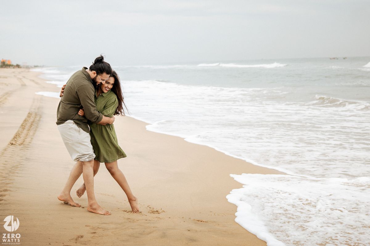 A couple walks along a serene beach shoreline during an overcast day.