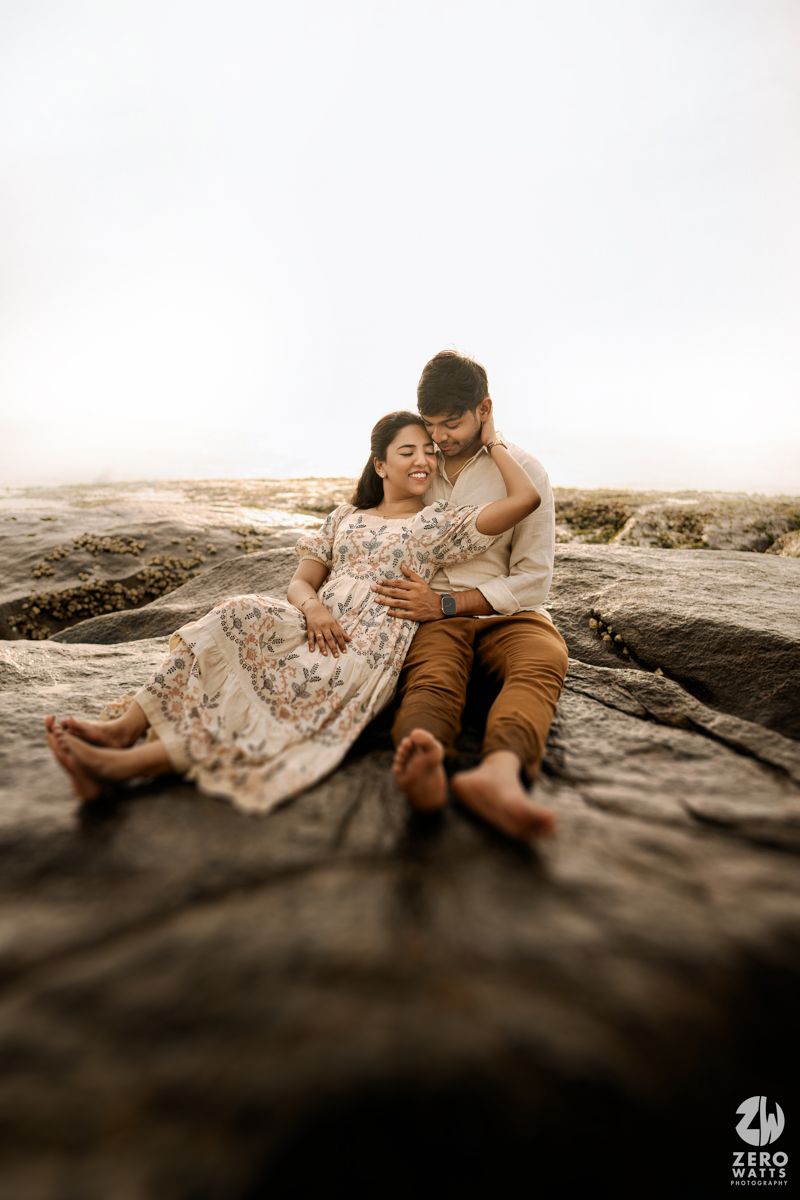 A romantic couple lying on rocky coastal terrain during a seaside photo session.