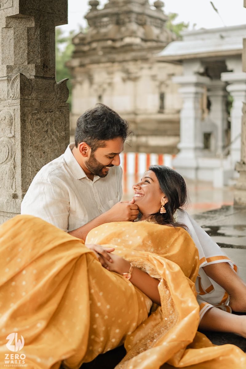 A romantic couple in traditional Indian attire share tender moments under ornate stone architecture.