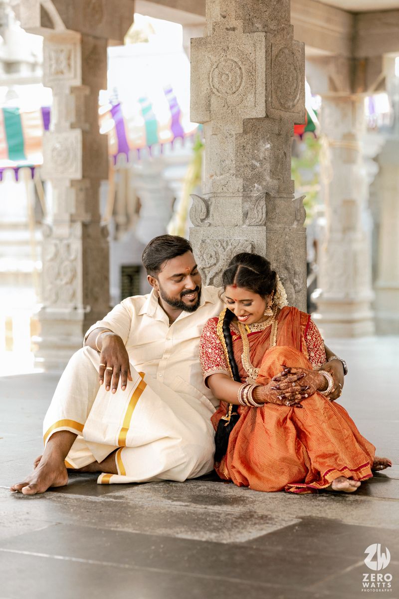 A couple in traditional Indian attire shares intimate moments while lying on a stone floor in a temple-like setting.