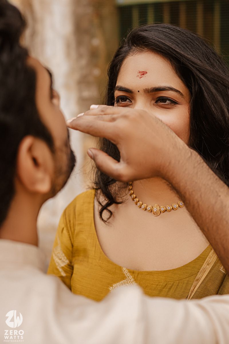 A couple in traditional Indian attire poses intimately against a warm-toned background with golden hues.