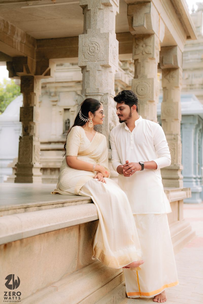 Couple in cream-colored traditional wear share tender moments along a temple corridor.