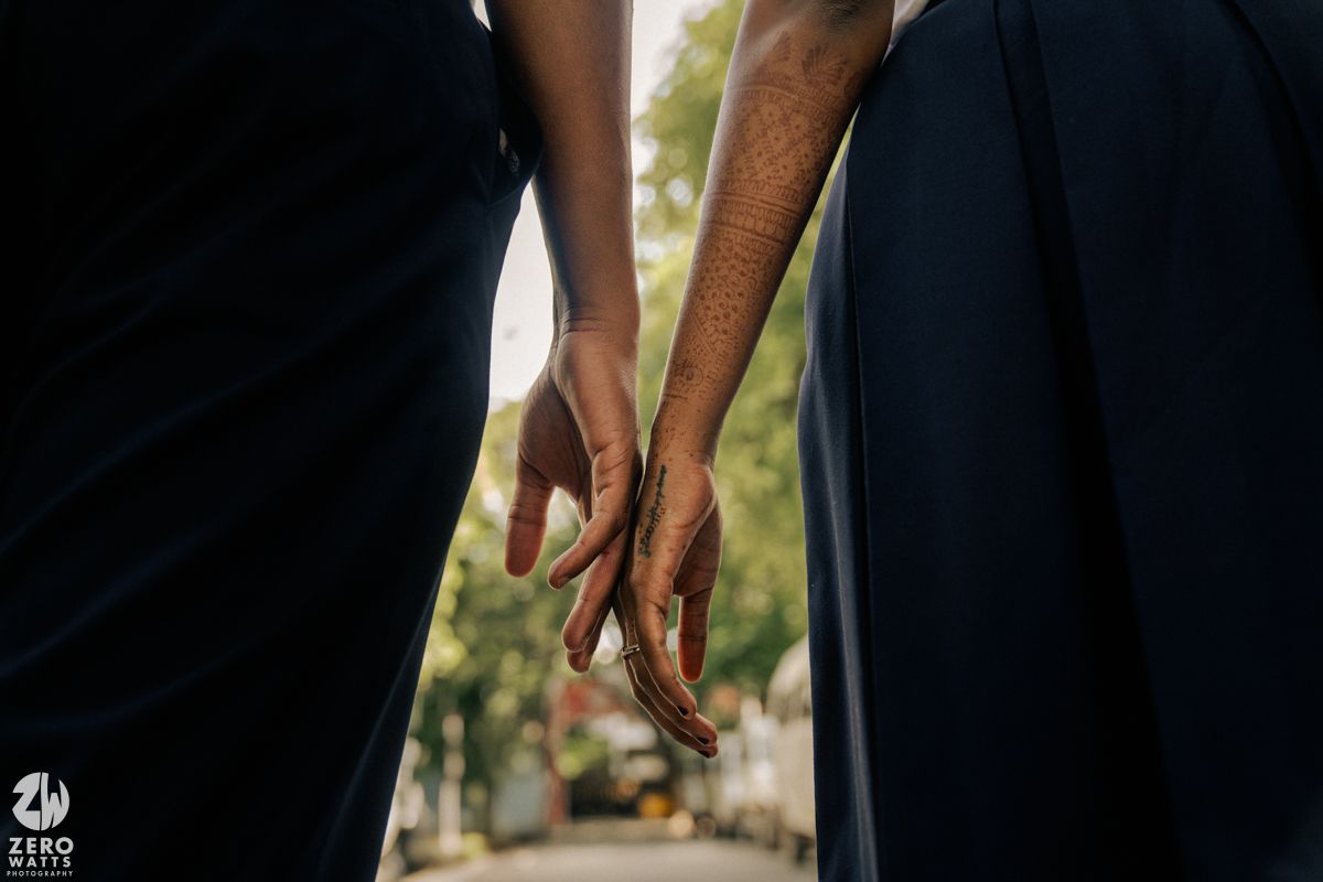Close-up shot of hands reaching for each other against dark clothing.