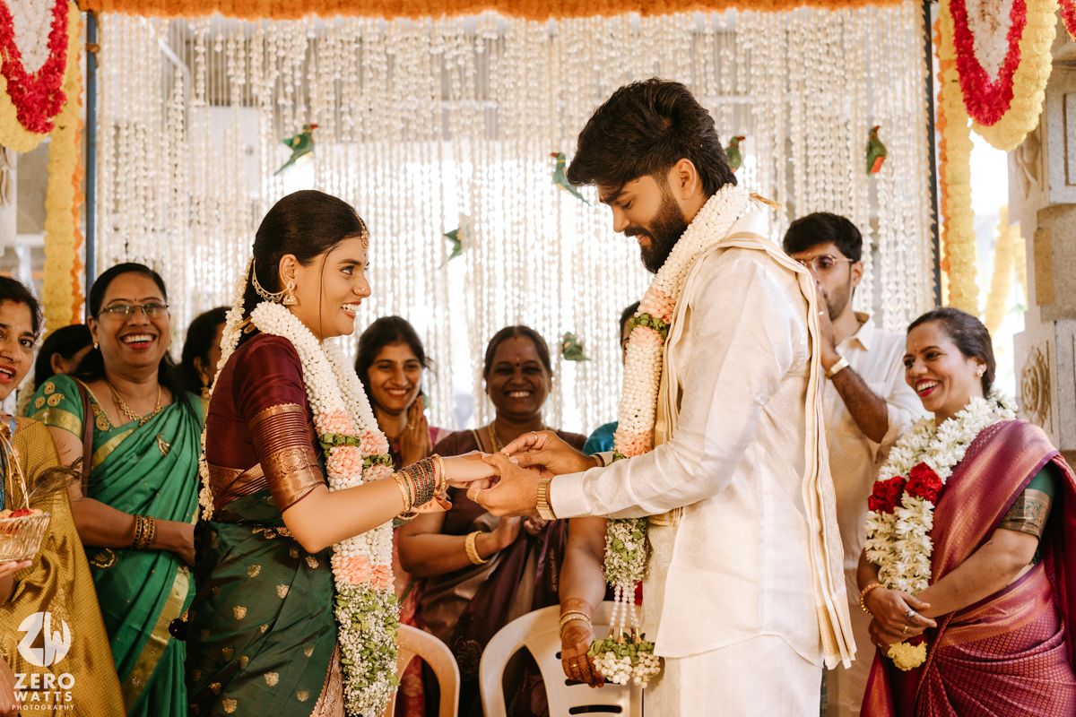 Traditional South Indian wedding ceremony with bride in green saree and groom in white exchanging rings.