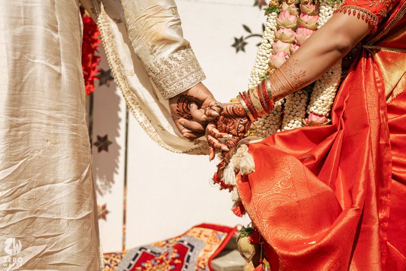 Close-up of bride and groom holding hands showcasing mehndi and bangles at a South Indian wedding.