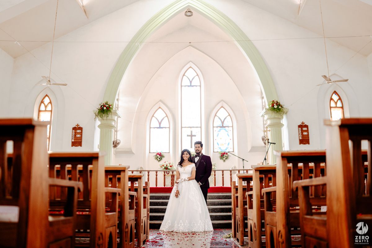 Bride and groom standing at the altar of a white church with wooden pews and stained glass windows.