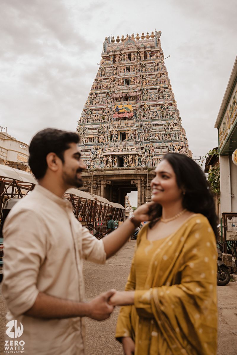 A couple poses in traditional Indian attire in front of an ornate temple gopuram with intricate architectural details.