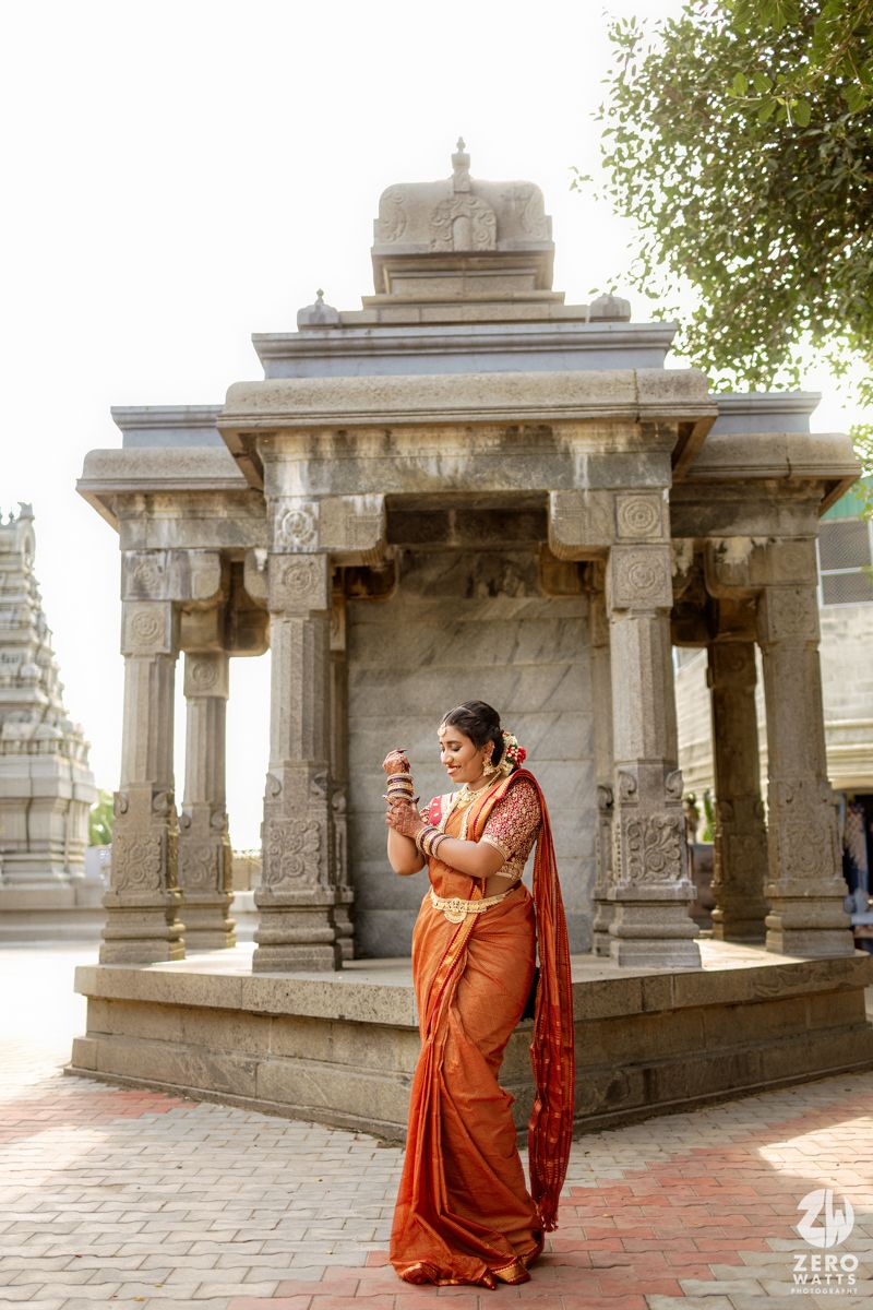 Ancient stone pillars and archways of a traditional temple courtyard with a figure in orange traditional attire.