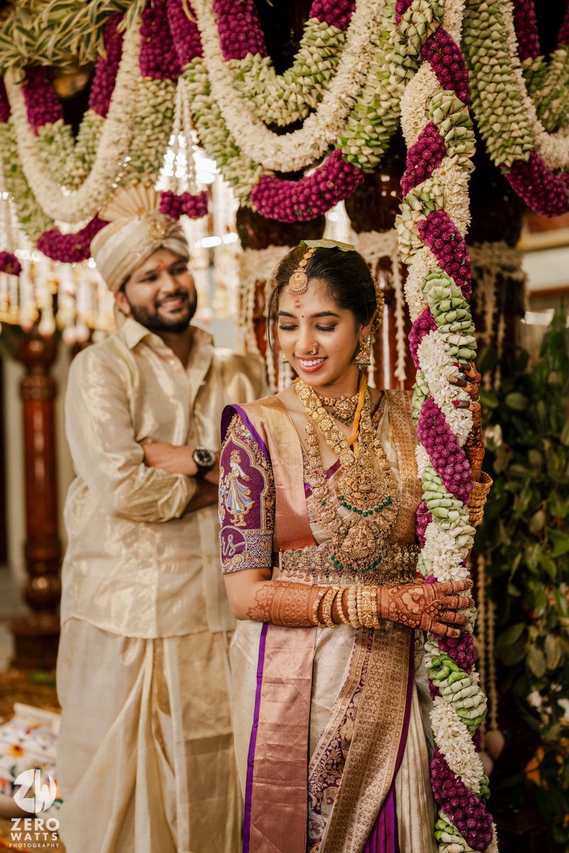 Candid moment of couple in traditional Indian wedding attire under mandap with pink and white flower garlands.