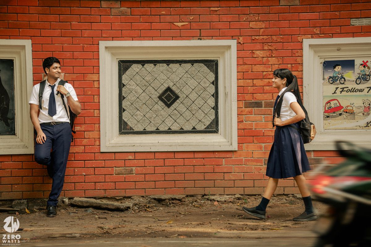 Students in school uniforms walking and talking along a brick wall corridor during daytime.