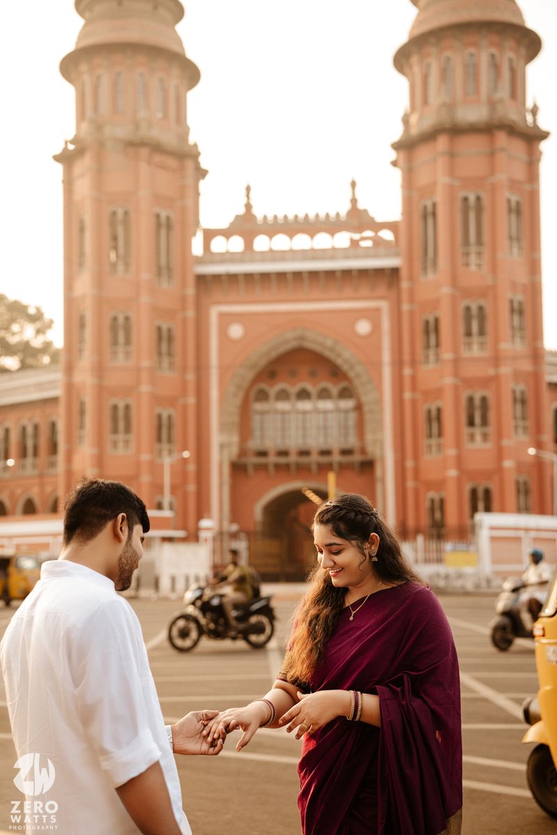 A couple poses in front of the historic red sandstone architecture of Chhatrapati Shivaji Terminus in Mumbai during sunset.