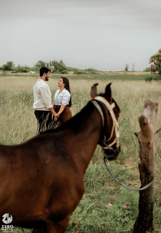 A romantic couple shares a tender moment on horseback in a serene field of tall grass at sunset.