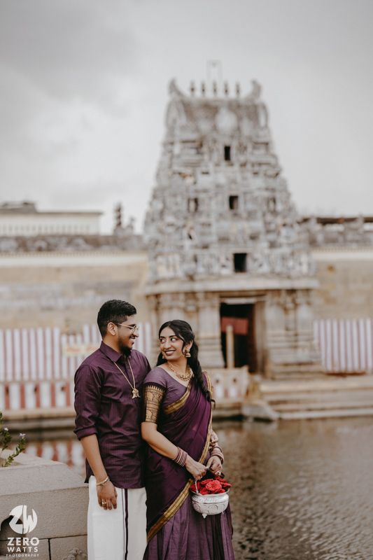 Couple in matching purple outfits poses at ancient temple complex with traditional architecture.
