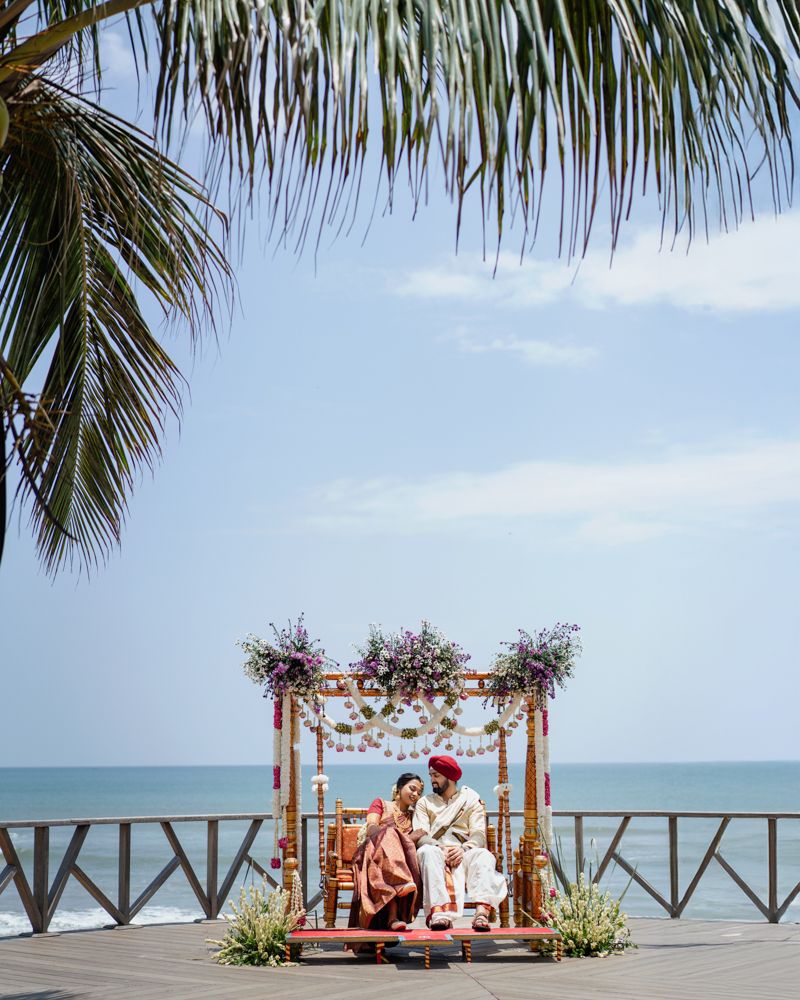 Tropical beachfront wedding ceremony setup with wooden pergola and palm trees overlooking the ocean.