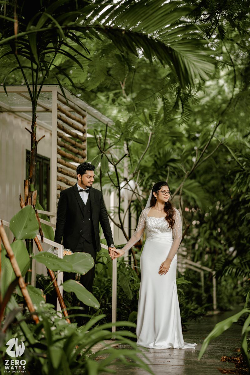 Bride and groom pose elegantly among lush tropical greenery in a romantic garden setting.