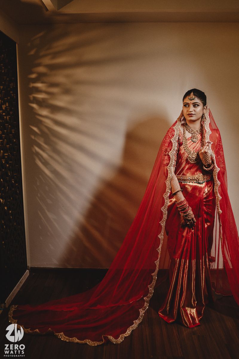 A traditional South Asian bride in a flowing red lehenga and veil poses elegantly against a neutral backdrop.