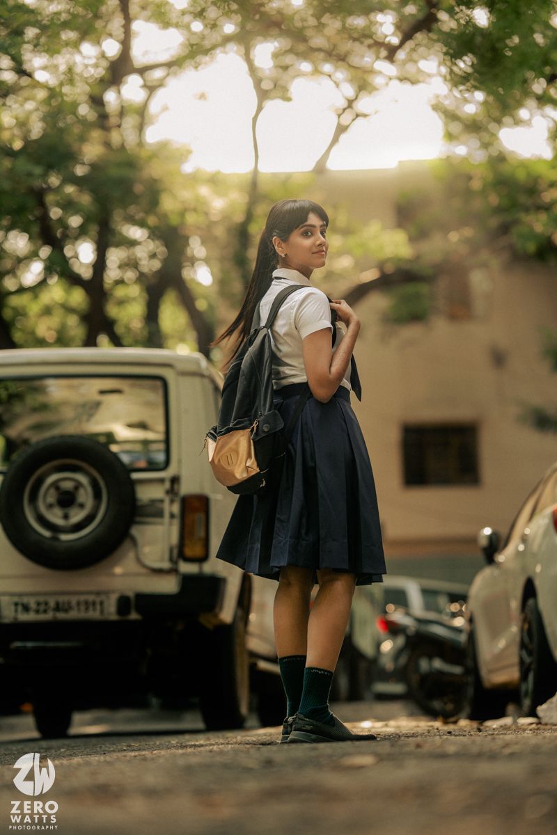 Student sitting alone outdoors with backpack against natural lighting and vintage cars in background.