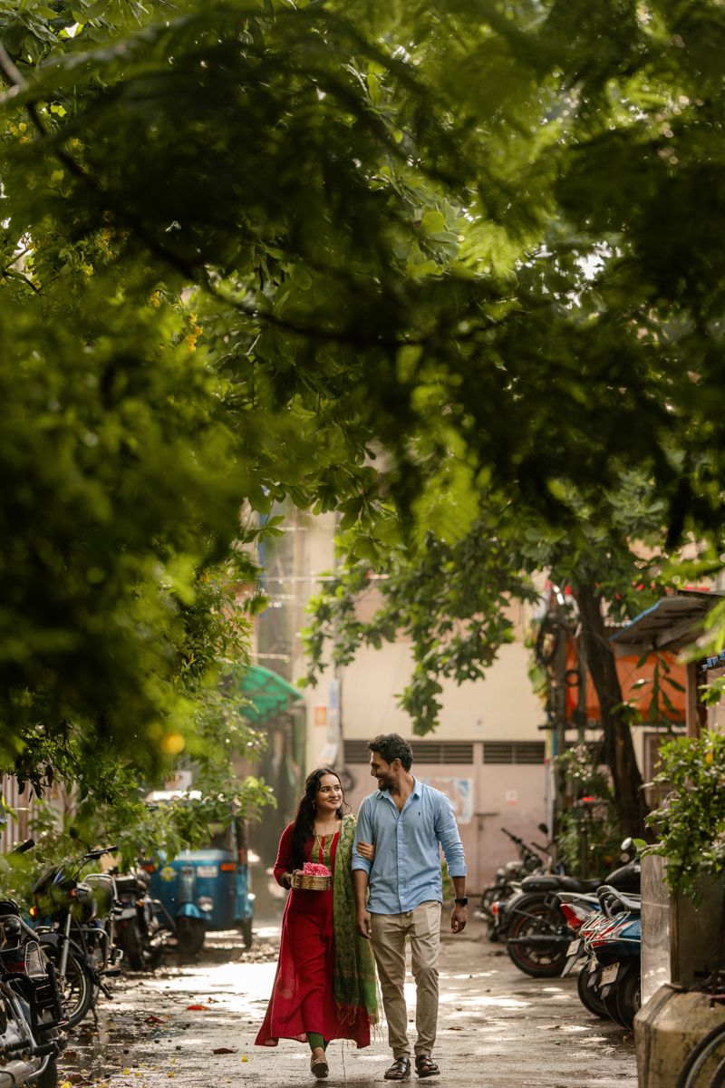 A couple strolls together under a canopy of green trees on a peaceful tree-lined street.