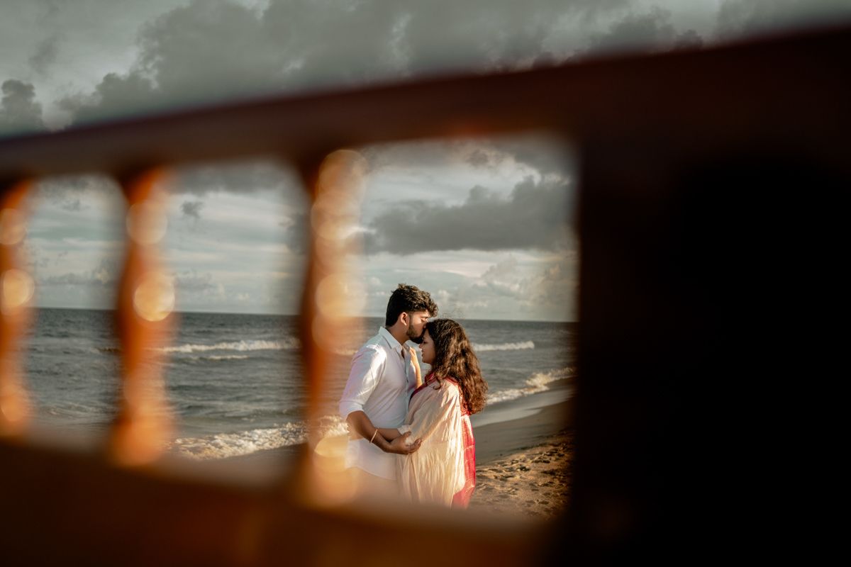 Creative beach portrait framed through wooden slats showing waves and cloudy sky in background.