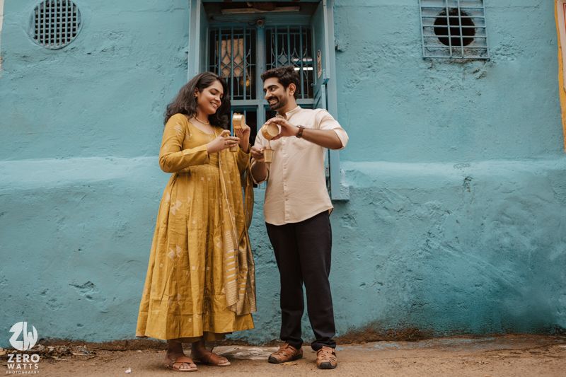 A couple stands together against a turquoise blue wall in an artistic photoshoot.