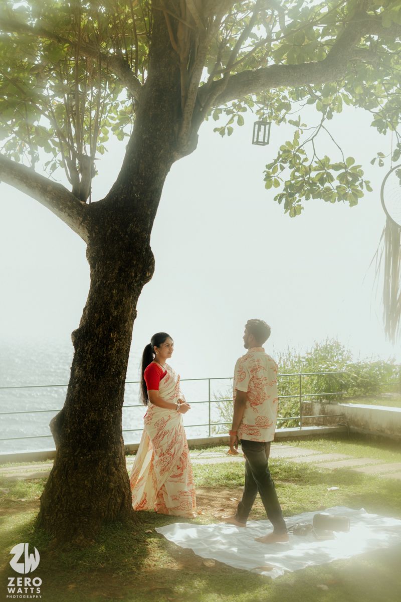 A dreamy scene under a large tree by the ocean with a couple sharing an intimate moment.