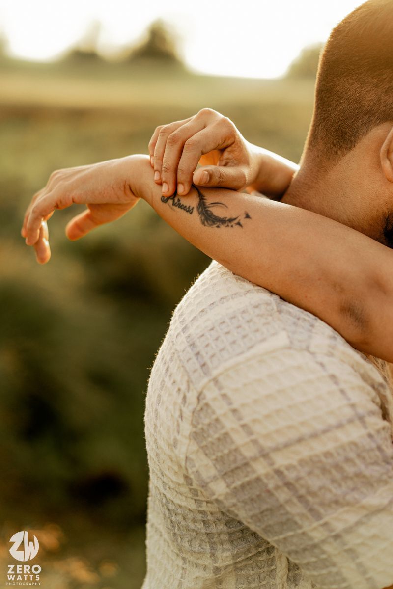 Close-up of hands with delicate tattoos against a white textured fabric in warm sunlight.