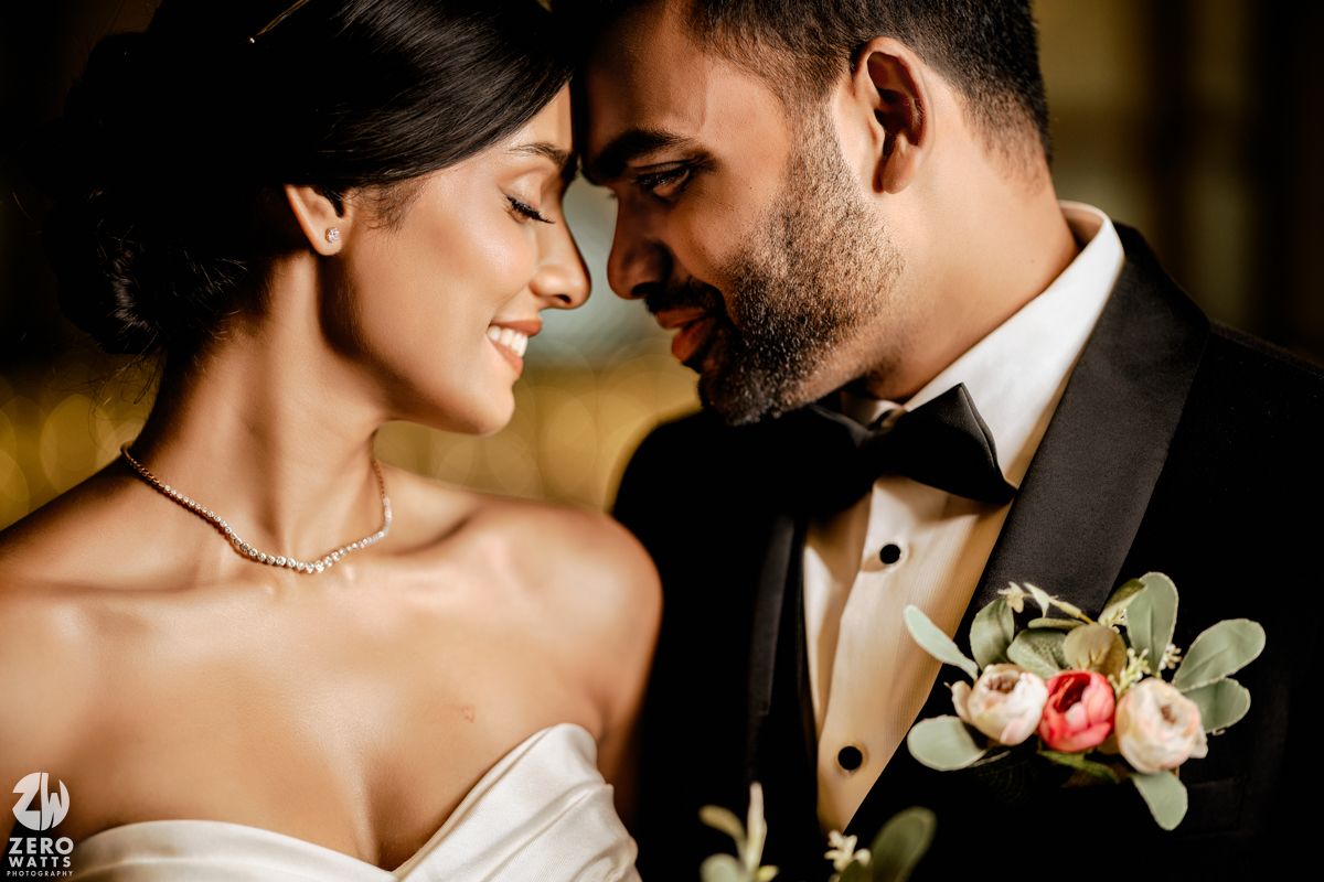 Bride and groom share intimate moment, smiling close together, groom wearing floral boutonniere.
