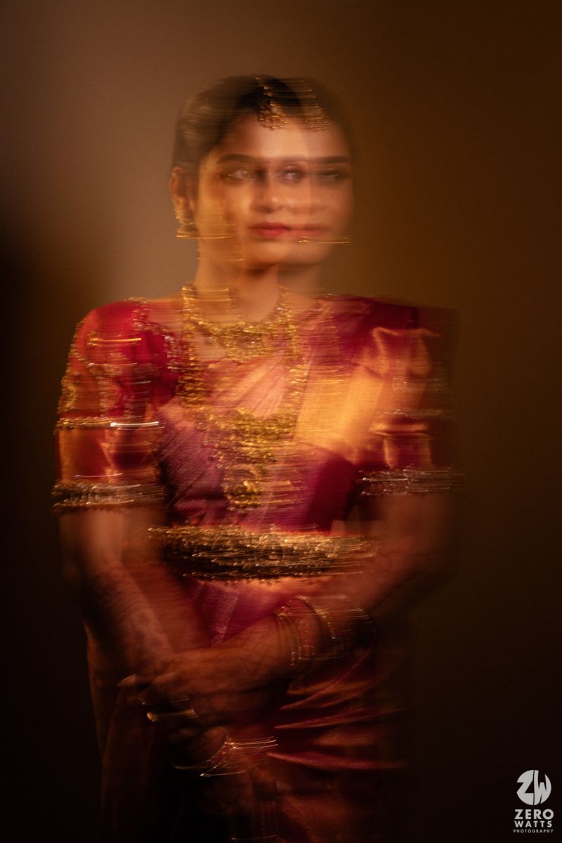 Blurred motion portrait of a South Indian bride in red silk saree with gold jewelry.