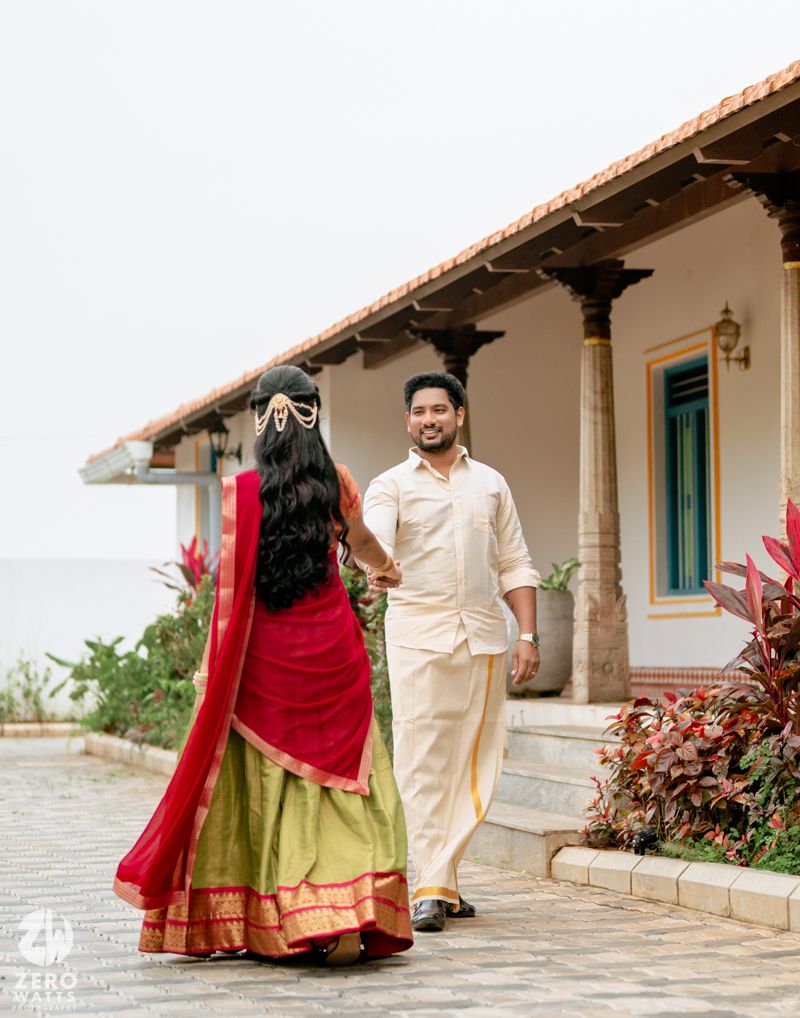South Indian couple in traditional wedding attire walking together outside a heritage villa.