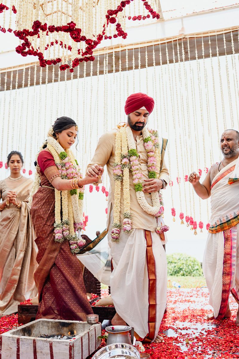 Traditional Indian wedding ceremony with couple performing ritual on red rose petal covered floor.