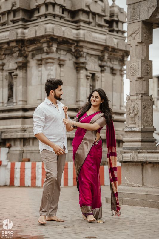 Couple in traditional attire dancing and posing together at a temple with ornate stone pillars in the background.