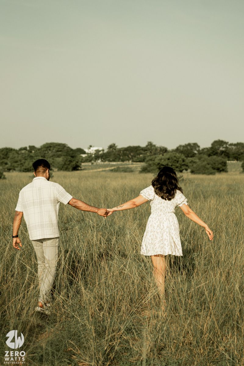 Two people holding hands while walking through a serene meadow with tall grass.