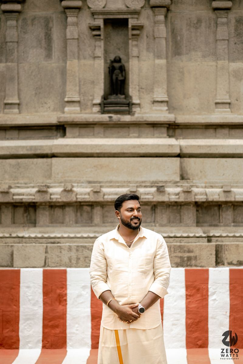 A person in a light-colored shirt stands in front of a stone building with red and white striped barriers.