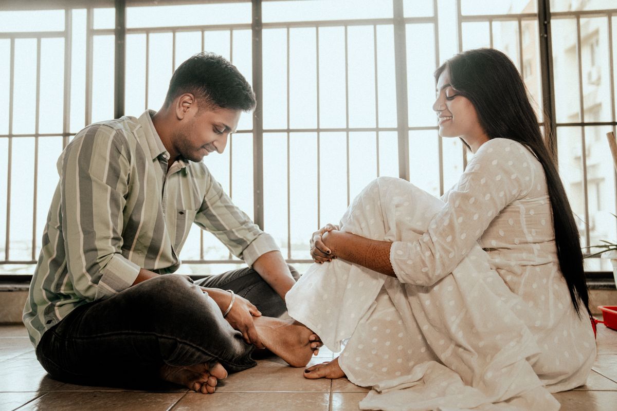 Couple in white outfits posing together near large windows during a photoshoot.