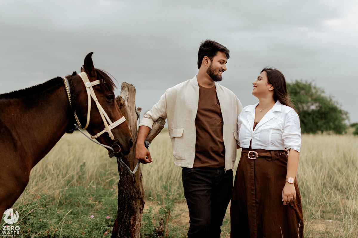 A couple shares an intimate moment beside their horse in a rustic field setting.