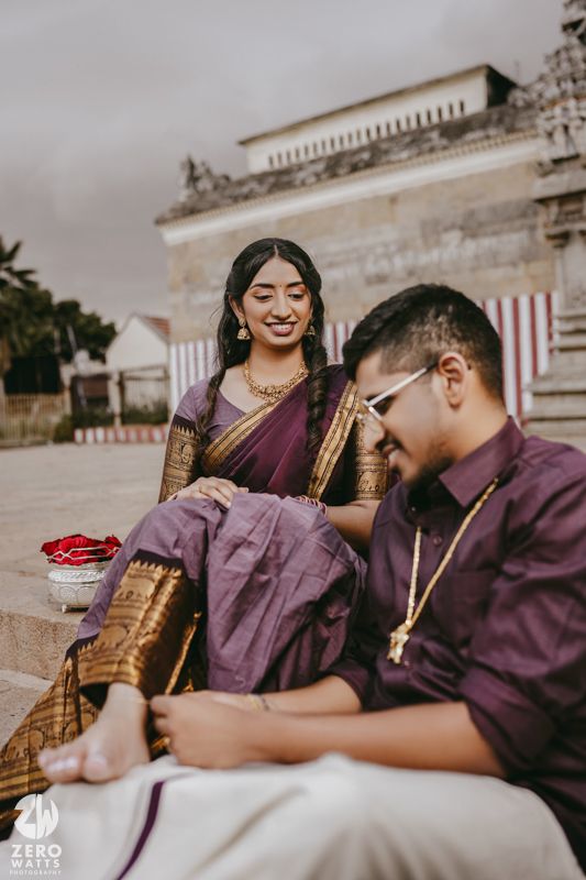 Candid moments of a couple in coordinated purple outfits sitting by a temple pond.