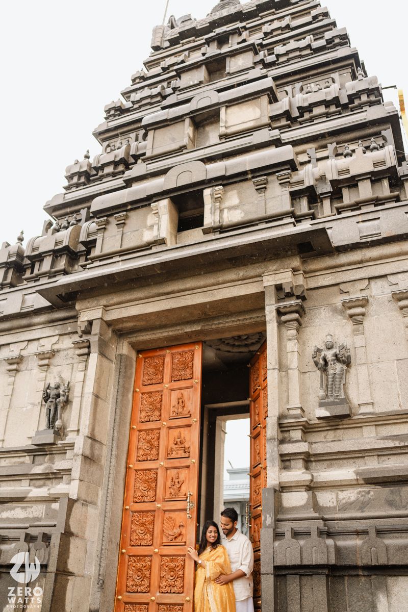 Ancient stone temple with ornate orange wooden doors and traditional South Indian architecture details in gray stone.